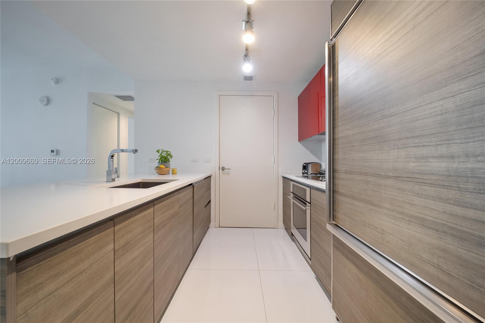A galley kitchen features wood-grain cabinets, white countertops, red upper cabinets, and white tile flooring — 1100 Miami Ave # 2808, Miami FL 33130, MIAMI, FL