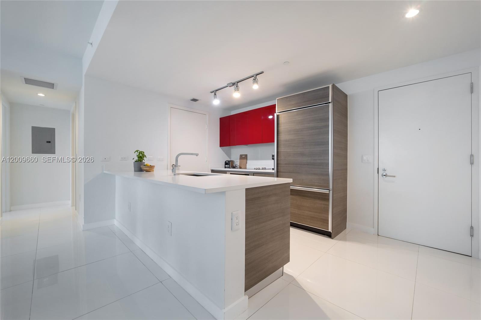 A modern kitchen features white countertops, wood-grain cabinetry, red upper cabinets, and white tile flooring — 1100 Miami Ave # 2808, Miami FL 33130, MIAMI, FL