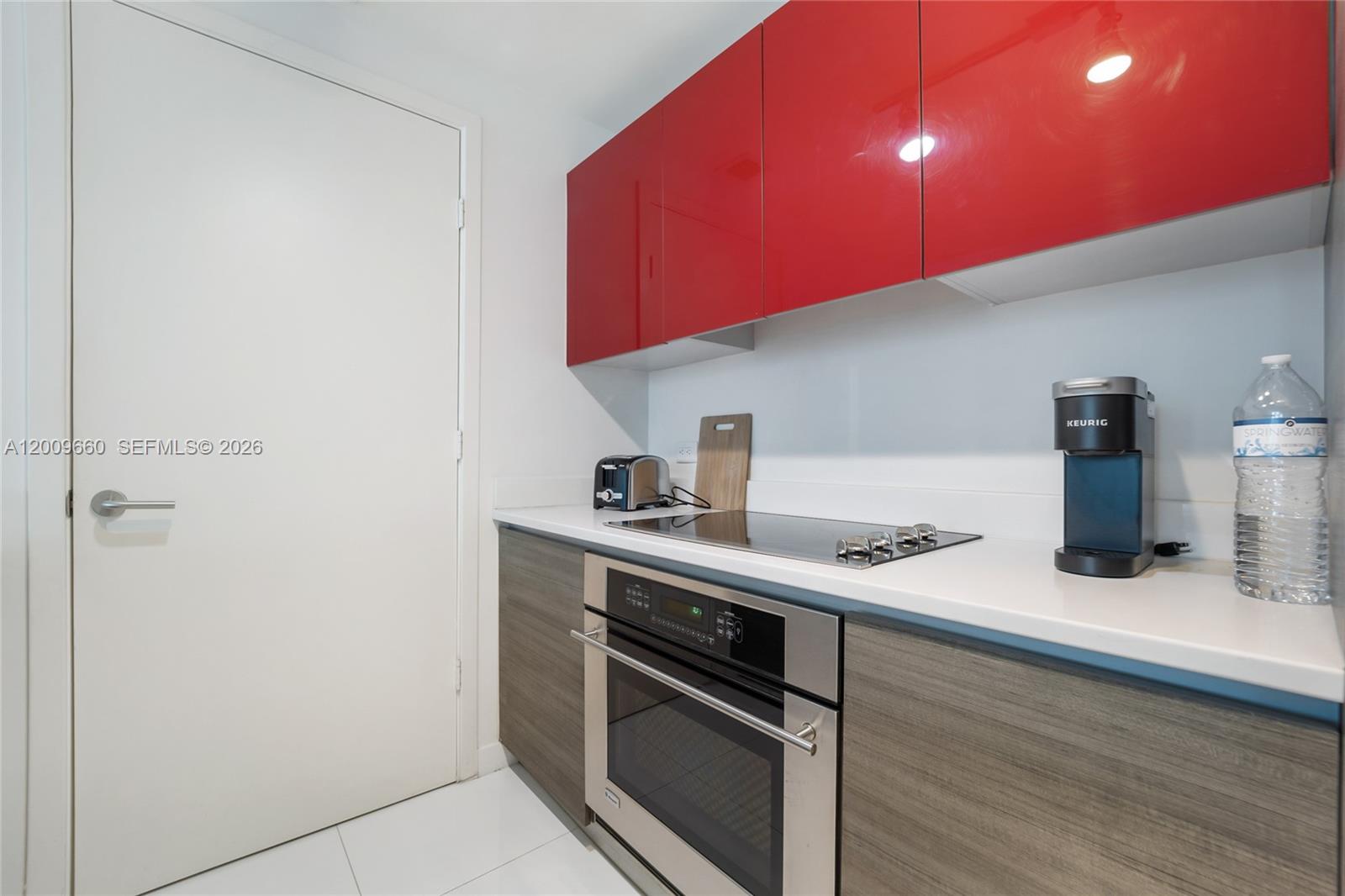 A modern kitchen features red upper cabinets, wood-grain lower cabinets, and stainless steel appliances — 1100 Miami Ave # 2808, Miami FL 33130, MIAMI, FL