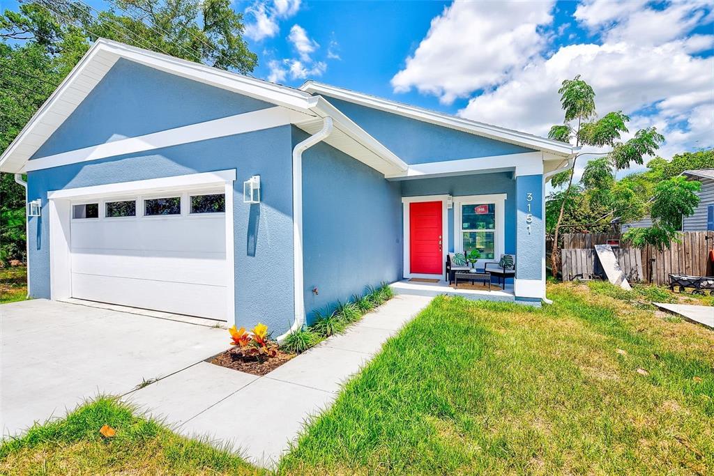 A blue single-story house features a white garage door, a bright red front door, and a walkway — 3151 69TH AVENUE N, ST PETERSBURG, FL