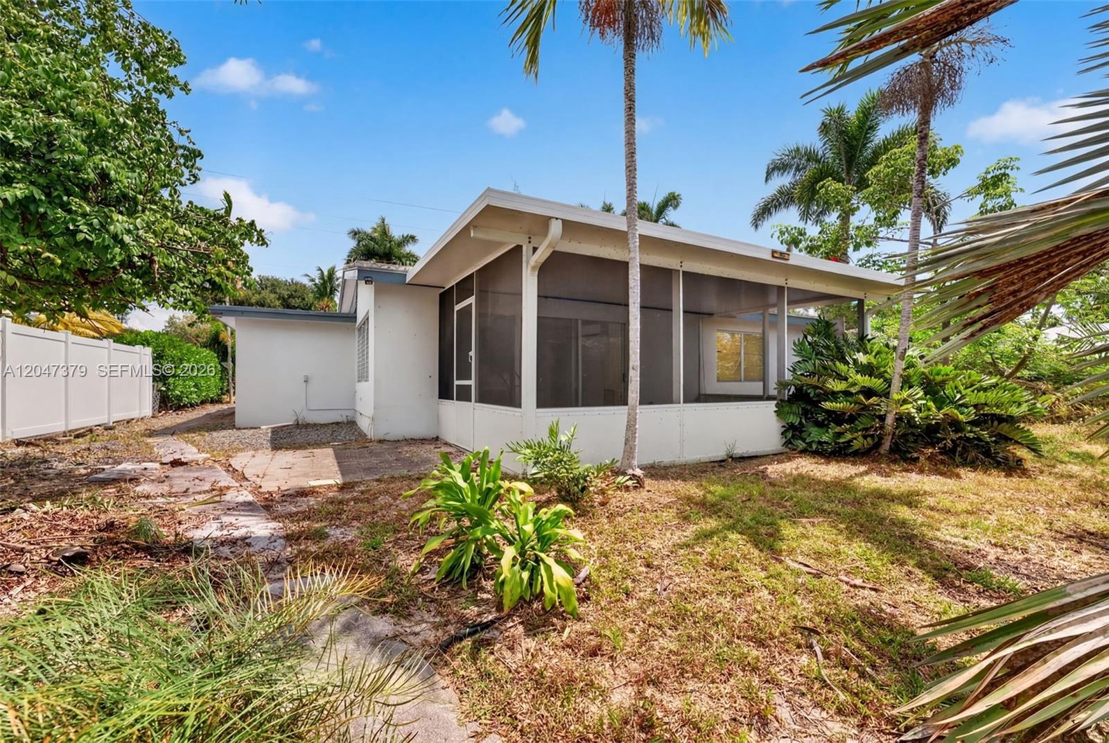 A white house features a screened-in porch and a paved patio area in the backyard — 2472 SE 13th Ct, Pompano Beach FL 33062, POMPANO BEACH, FL
