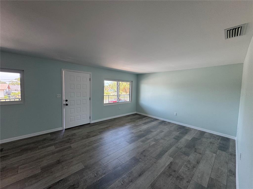 An empty room features light blue walls, gray wood-look flooring, a white door, and windows — 1258 BARBARA DRIVE UNIT 202, VENICE, FL