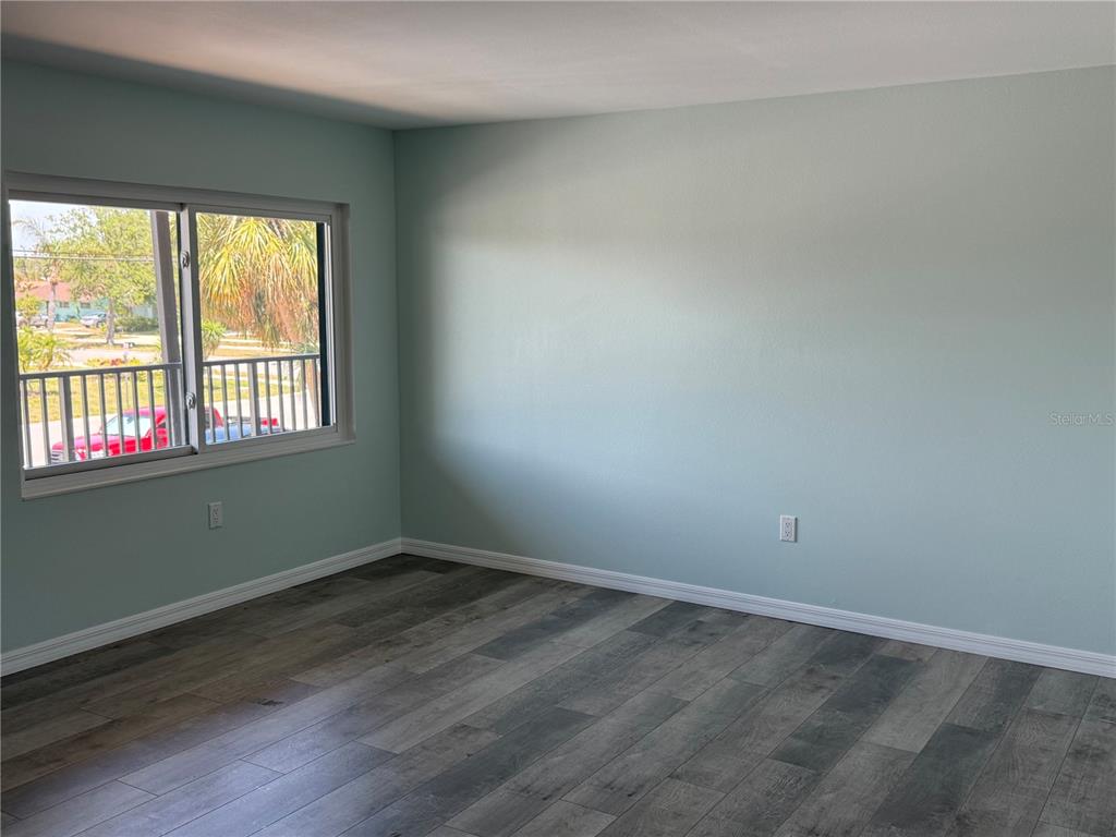 An empty room features light blue walls, gray wood-look flooring, and a large window — 1258 BARBARA DRIVE UNIT 202, VENICE, FL