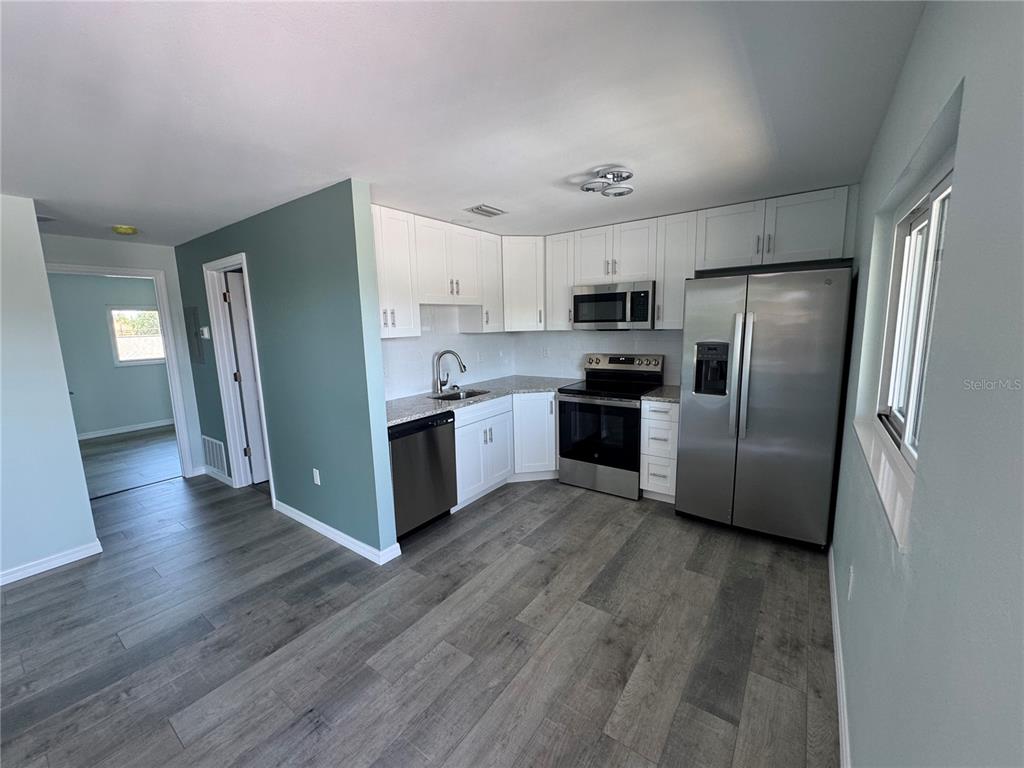 A kitchen features white cabinets, stainless steel appliances, granite countertops, and gray wood-look flooring — 1258 BARBARA DRIVE UNIT 202, VENICE, FL