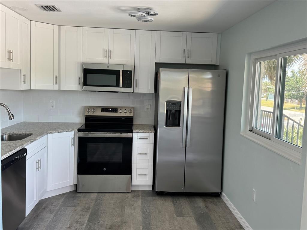 A kitchen features white cabinets, stainless steel appliances, granite countertops, and wood-look flooring — 1258 BARBARA DRIVE UNIT 202, VENICE, FL