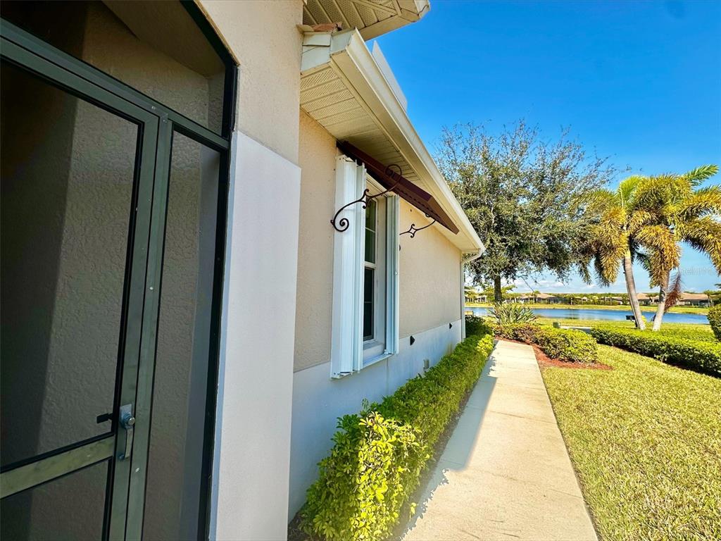A side view of a house exterior with a walkway, landscaping, and a lake view — 10726 CETRELLA DRIVE, FORT MYERS, FL