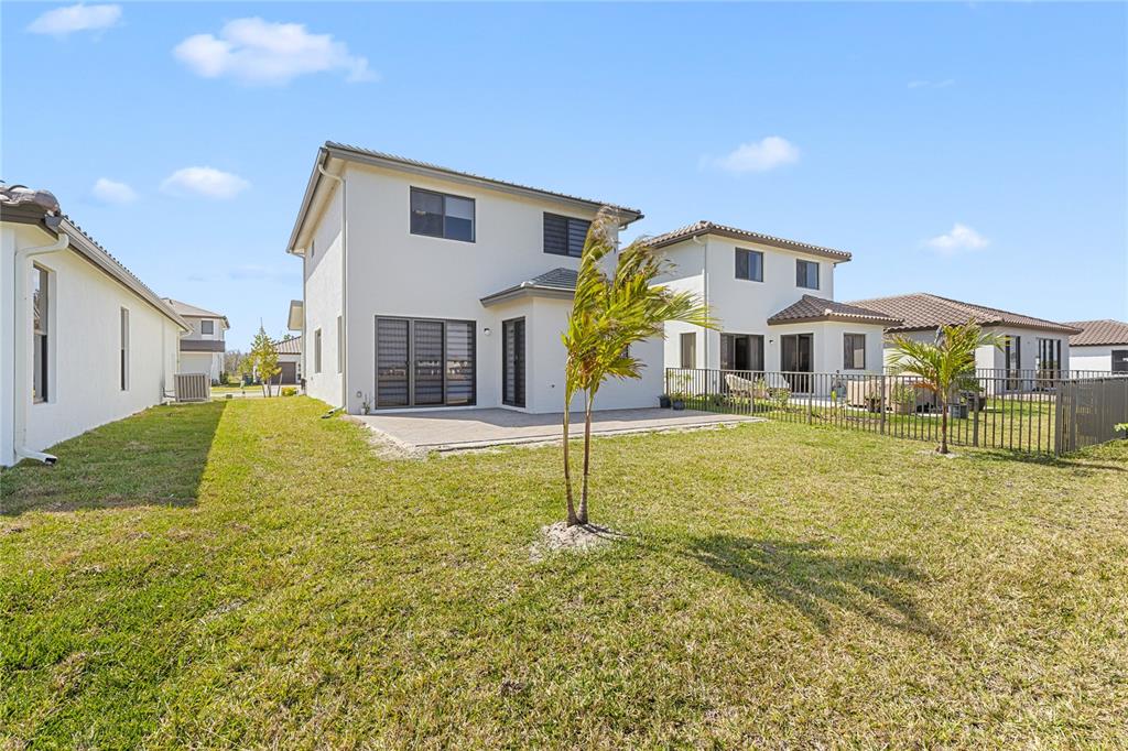 The rear exterior of a two-story house features a patio, lawn, and metal fencing — 5771 AGOSTINO WAY, AVE MARIA, FL