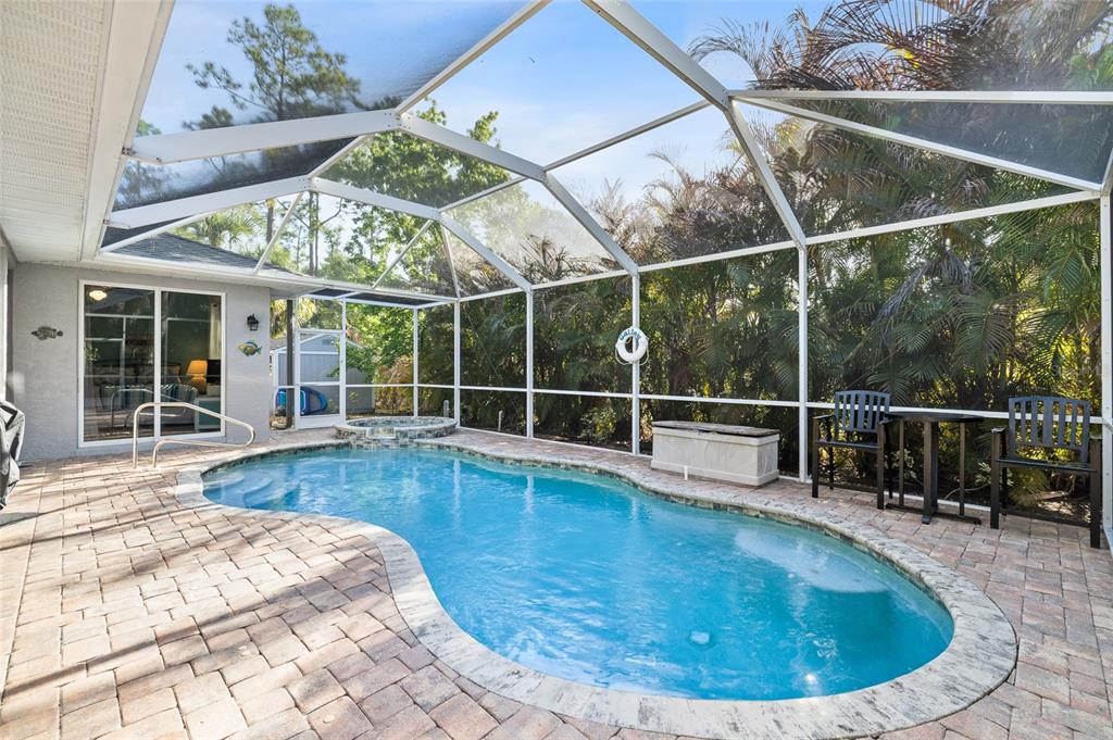 A screened-in patio features a kidney-shaped swimming pool, a hot tub, and paver flooring — 3730 CRANDON ROAD, NORTH PORT, FL