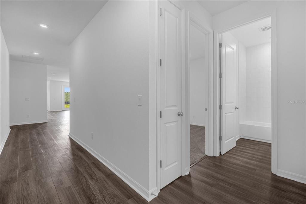 A hallway with wood-look flooring leads to a bathroom and an open living area — 2355 LANCASHIRE STREET, DAVENPORT, FL