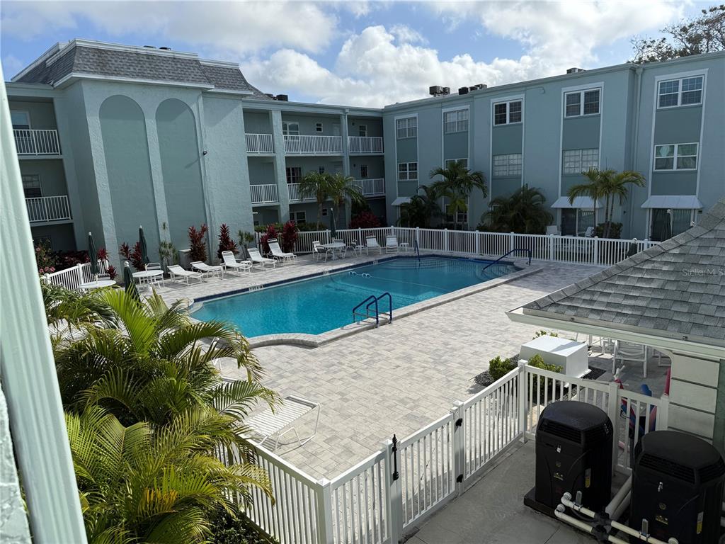 An outdoor swimming pool surrounded by a paved deck and a multi-story apartment building — 1706 BELLEAIR FOREST DRIVE UNIT 226, BELLEAIR, FL