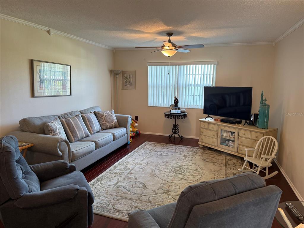 A living room features a grey sofa, two armchairs, a television, and a patterned area rug — 1706 BELLEAIR FOREST DRIVE UNIT 226, BELLEAIR, FL