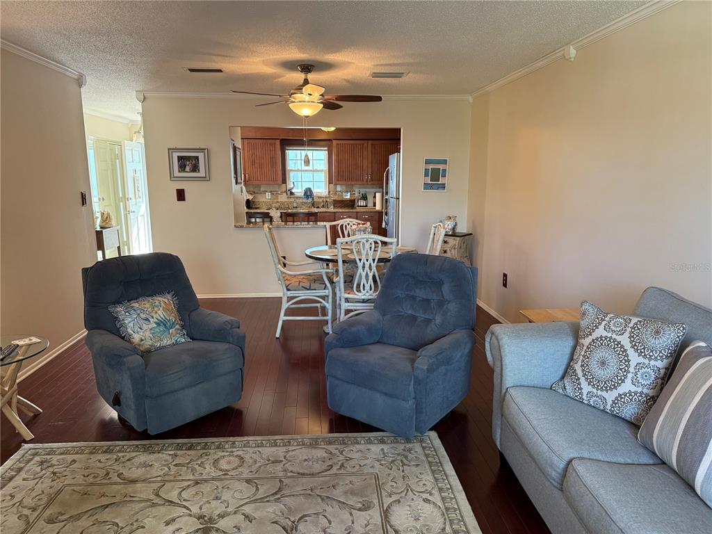 A living room with dark wood floors, two blue recliners, and a dining area beyond — 1706 BELLEAIR FOREST DRIVE UNIT 226, BELLEAIR, FL