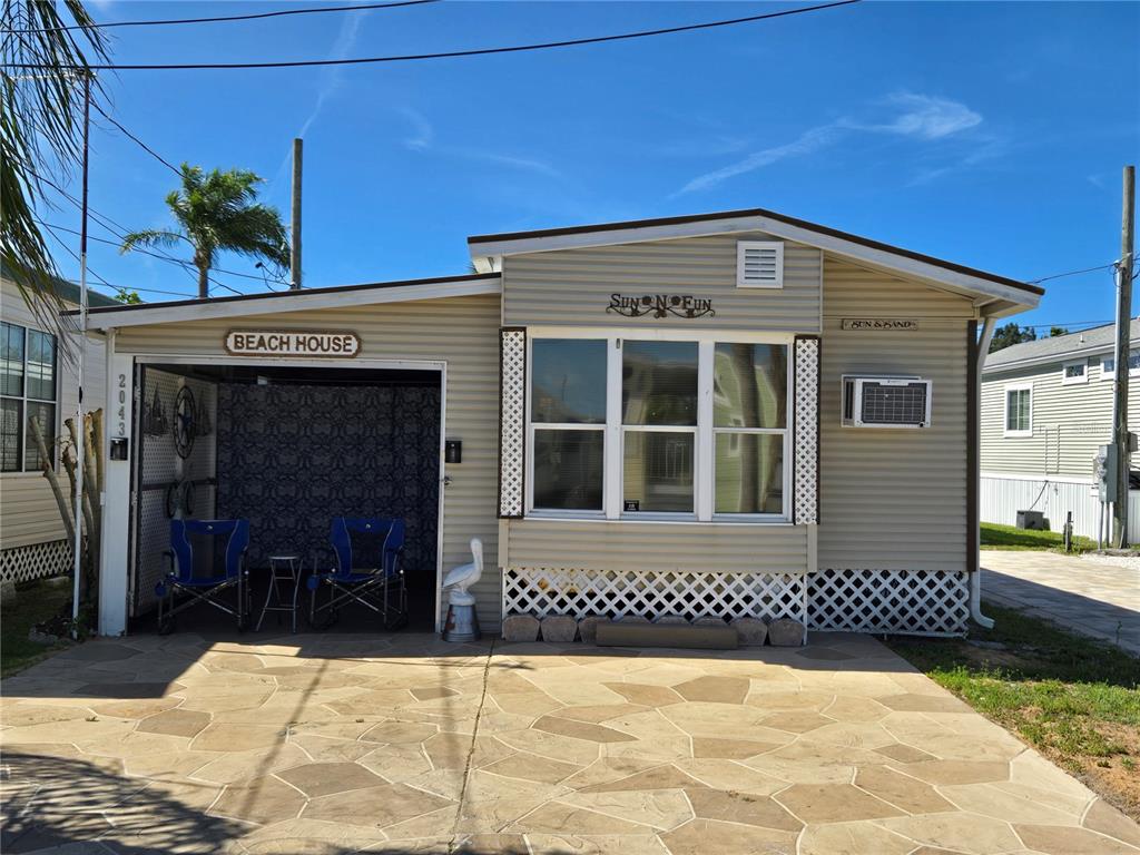 A single-story mobile home features a covered carport, beige siding, and a decorative lattice skirt — 2043 KETCH CIRCLE UNIT C7, PALM HARBOR, FL