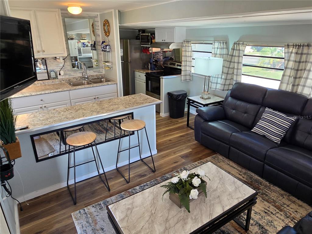 An open-concept living room and kitchen featuring a breakfast bar, dark sofa, and wood flooring — 2043 KETCH CIRCLE UNIT C7, PALM HARBOR, FL