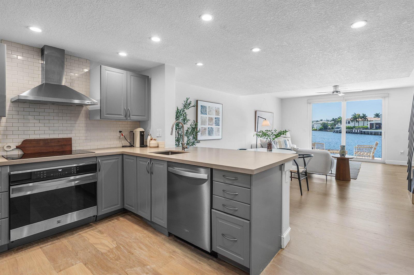 A modern kitchen with gray cabinets and stainless steel appliances overlooks a living area and water — 900 E Jeffery Street, Boca Raton FL 33487, BOCA RATON, FL