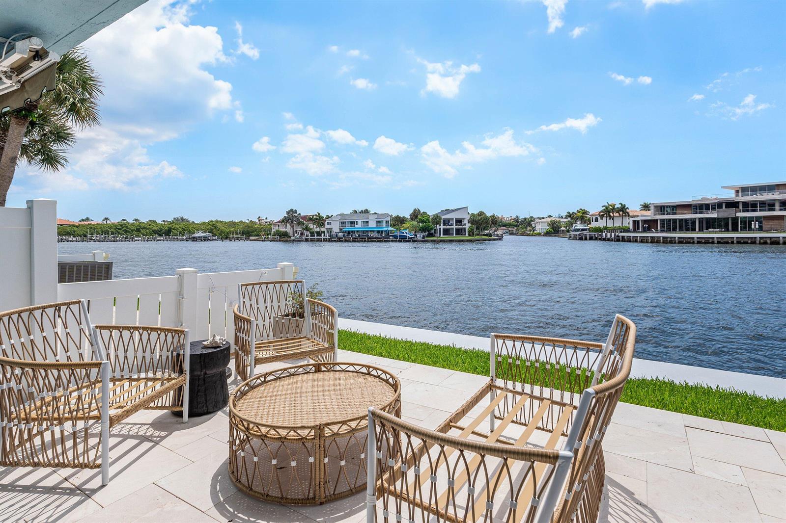 A patio with wicker furniture overlooks a canal lined with houses under a blue sky — 900 E Jeffery Street, Boca Raton FL 33487, BOCA RATON, FL