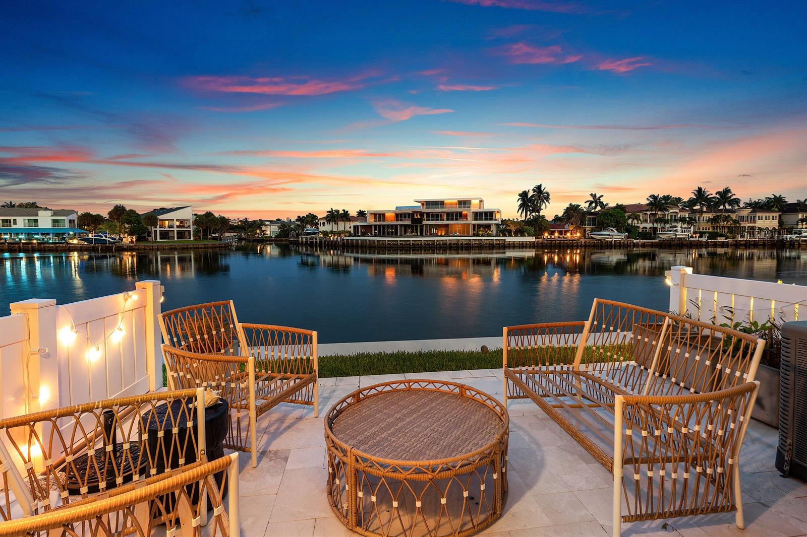 A patio with wicker furniture overlooks a calm canal at sunset with houses in background — 900 E Jeffery Street, Boca Raton FL 33487, BOCA RATON, FL