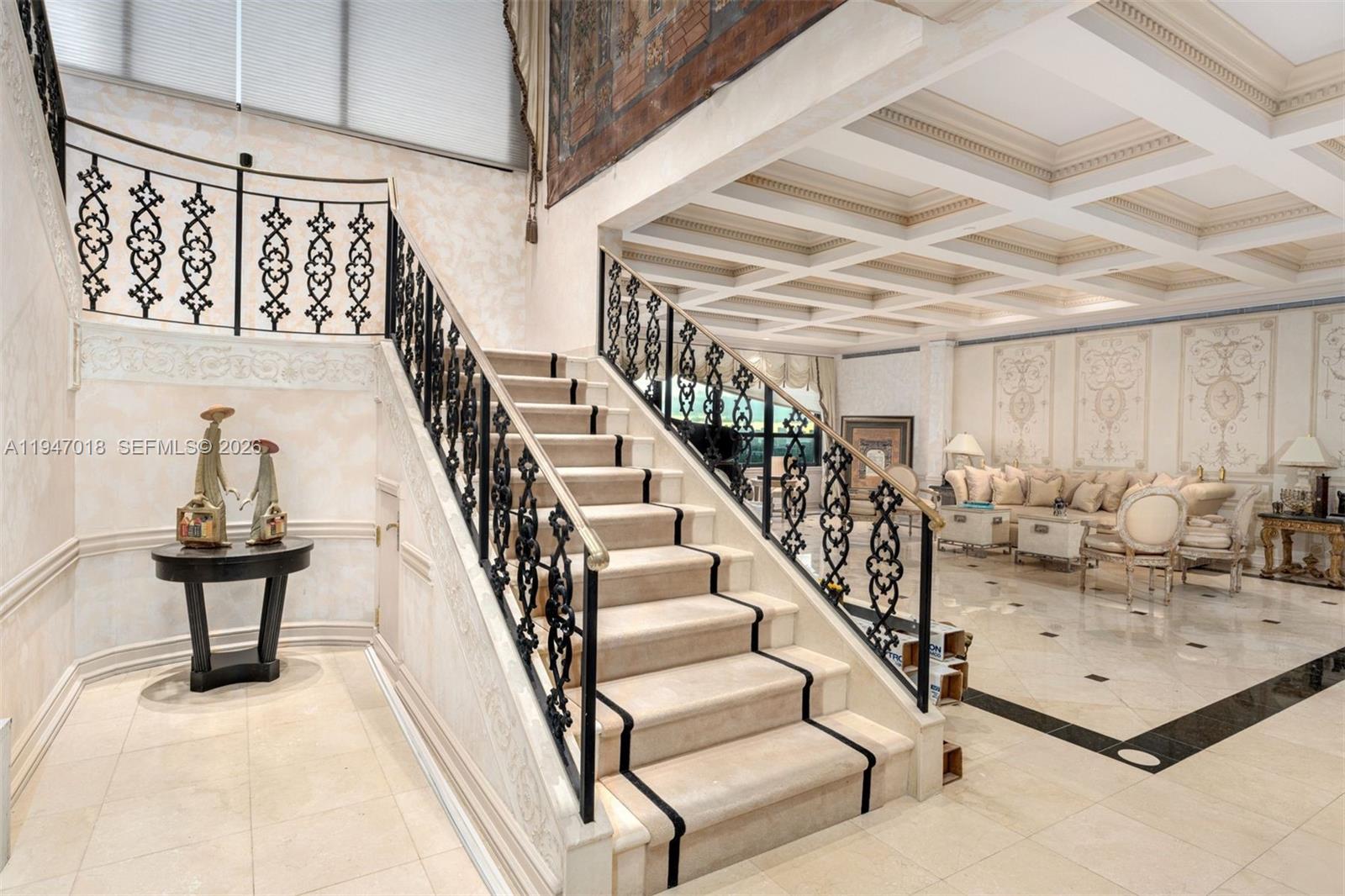 A grand staircase with ornate black railings leads to an upper level in a living room — 5225 Collins Ave, Miami Beach FL 33140, MIAMI BEACH, FL
