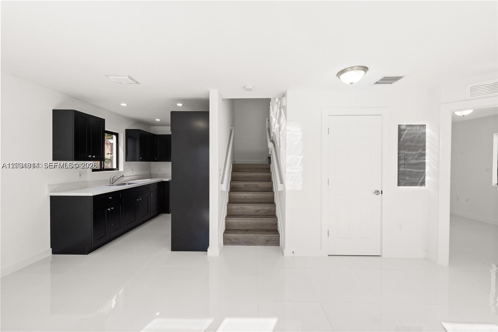 A kitchen with black cabinets and white countertops sits beside a staircase and doorway — 2243 NW 50th St # 2, Miami FL 33142, MIAMI, FL