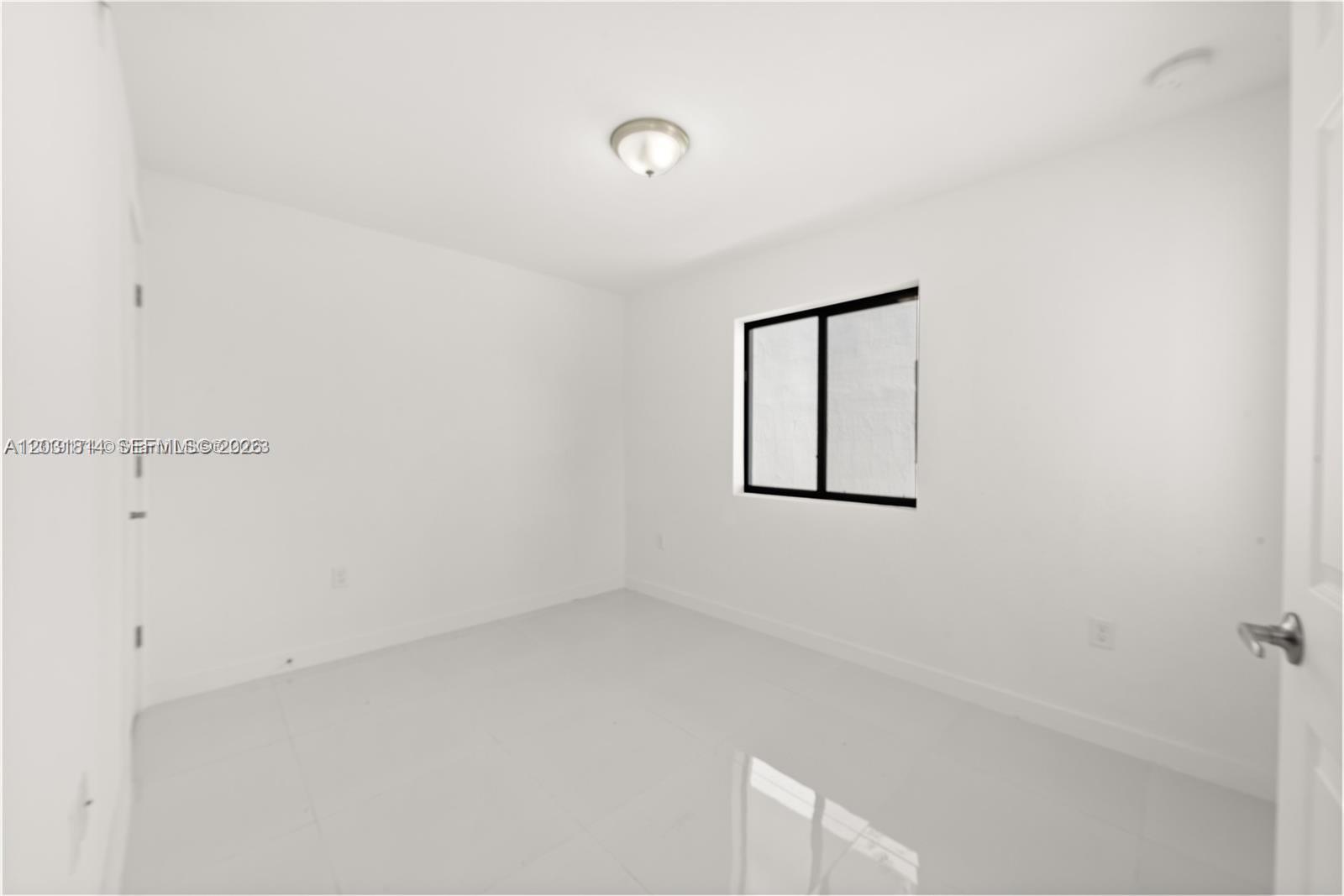 This is a small, empty bedroom with white walls, white tile flooring, and a single window — 2243 NW 50th St # 2, Miami FL 33142, MIAMI, FL