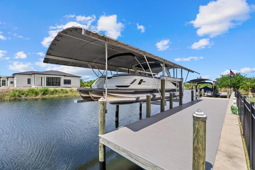 A pontoon boat sits on a lift under a canopy next to a wooden dock — 15672 LAKELAND CIRCLE, PORT CHARLOTTE, FL