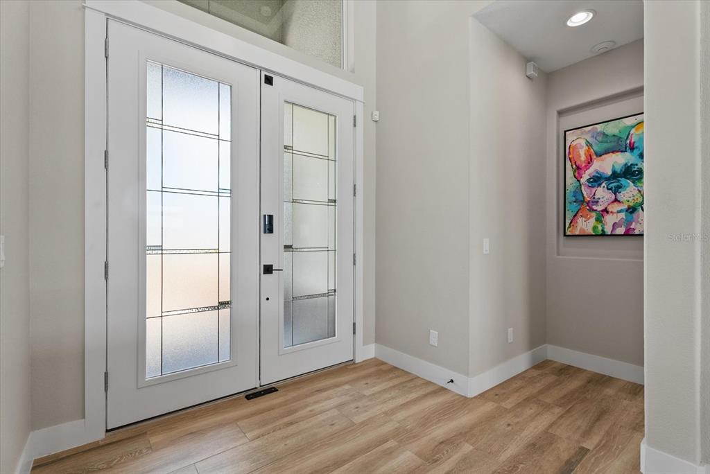 A bright entryway features double glass-paneled doors, light wood-look flooring, and a colorful dog painting — 15672 LAKELAND CIRCLE, PORT CHARLOTTE, FL