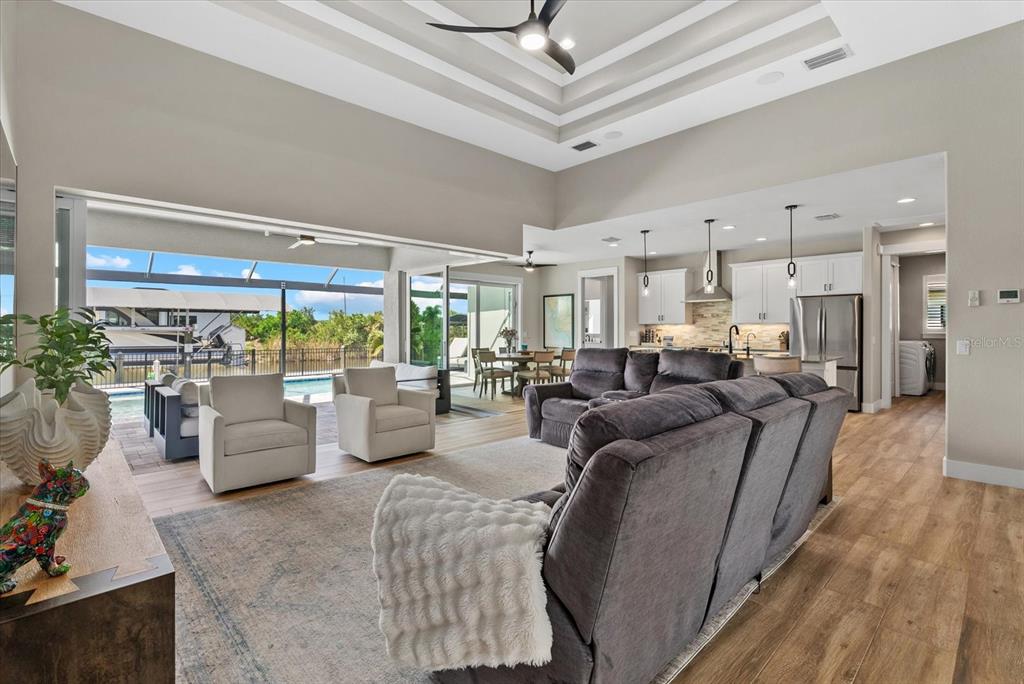 An open-concept living room and kitchen feature high tray ceilings, wood-look flooring, and sliding glass doors — 15672 LAKELAND CIRCLE, PORT CHARLOTTE, FL
