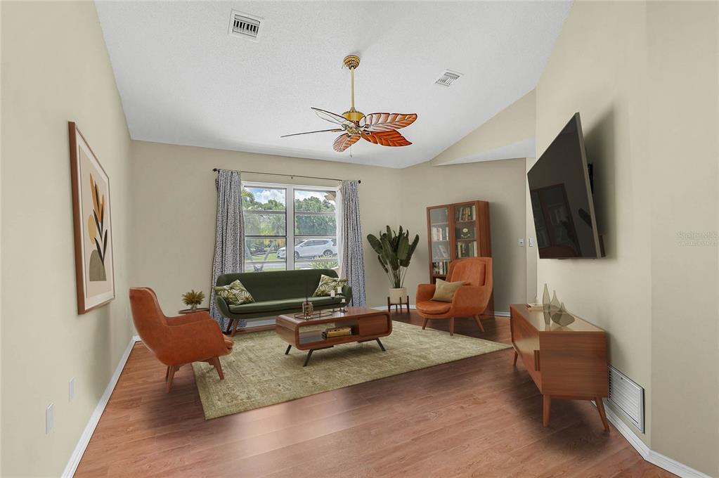 This living room features wood floors, a ceiling fan, and a green sofa with orange chairs — 5852 LINCOLN ROAD, VENICE, FL