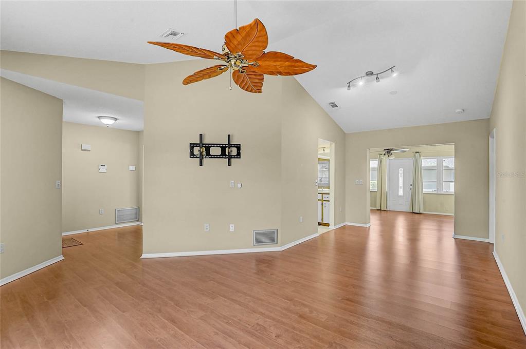 An empty living room features light-colored walls, wood-look flooring, and a palm-leaf ceiling fan — 5852 LINCOLN ROAD, VENICE, FL