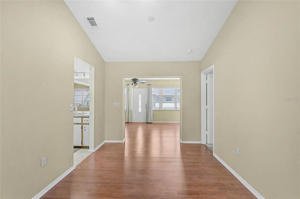 A view through a hallway with wood-look flooring toward an entryway with a front door — 5852 LINCOLN ROAD, VENICE, FL