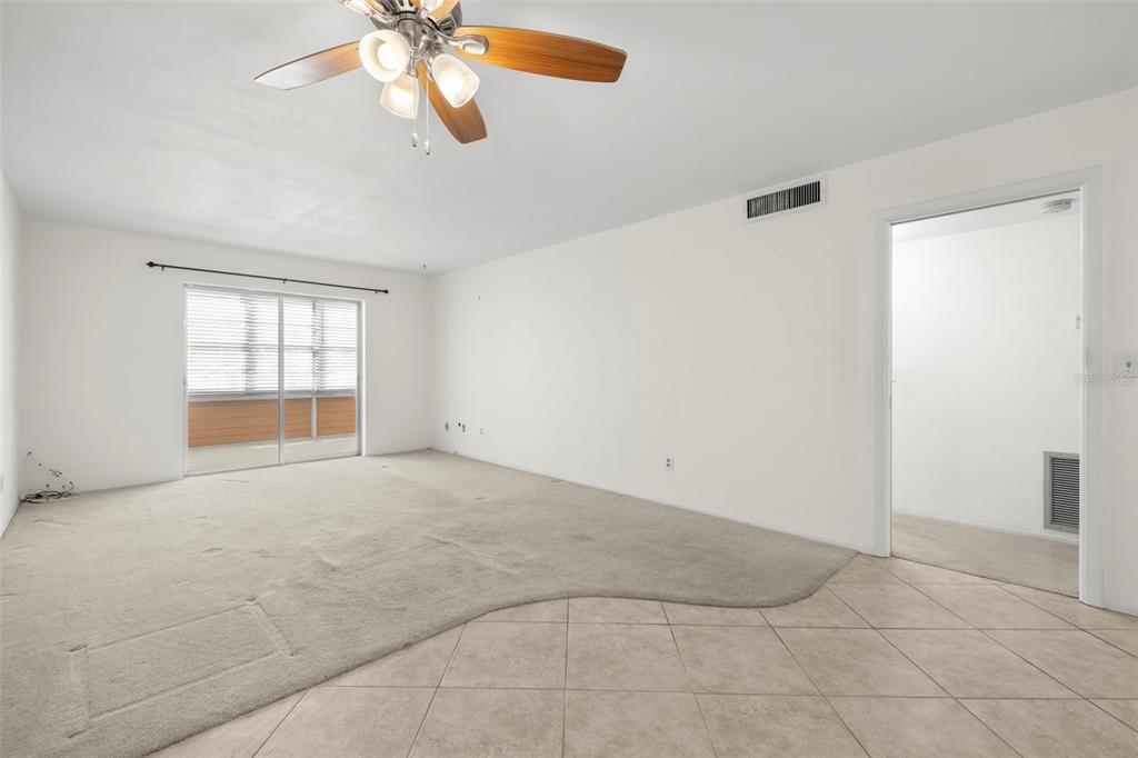 An empty living room features a ceiling fan, tiled entryway, and carpeted flooring — 400 GLENNES LANE UNIT 206, DUNEDIN, FL