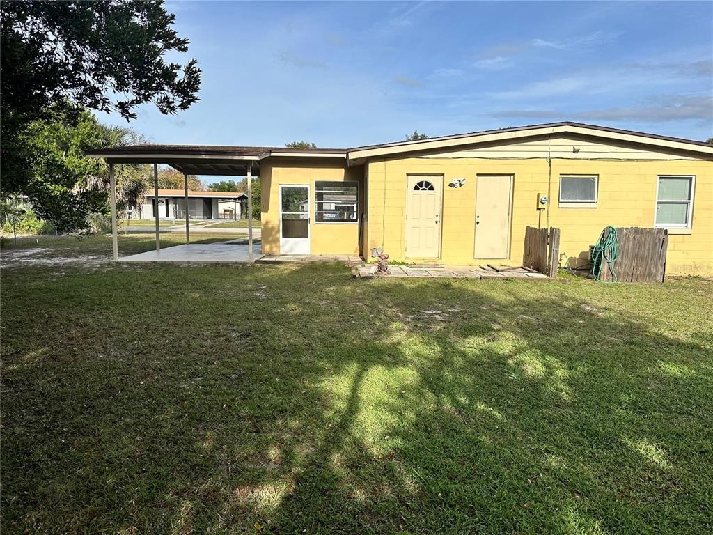 A yellow single-story house features a carport, two exterior doors, and a grassy backyard — 2302 IDAHO ROAD, DELTONA, FL