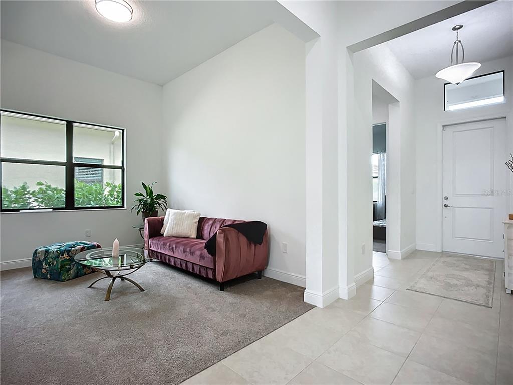 A living area with a velvet sofa, glass coffee table, and adjacent tiled entryway — 9132 BERNINI PLACE, SARASOTA, FL