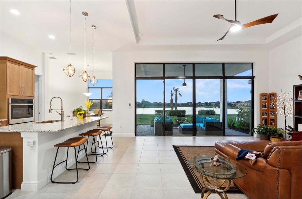 An open-concept kitchen and living area features a breakfast bar, tile floors, and large windows — 9132 BERNINI PLACE, SARASOTA, FL