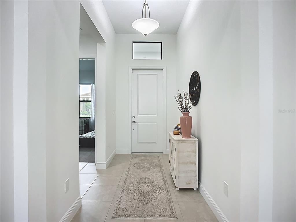 A bright entryway features a white door, a runner rug, and a light wood cabinet — 9132 BERNINI PLACE, SARASOTA, FL