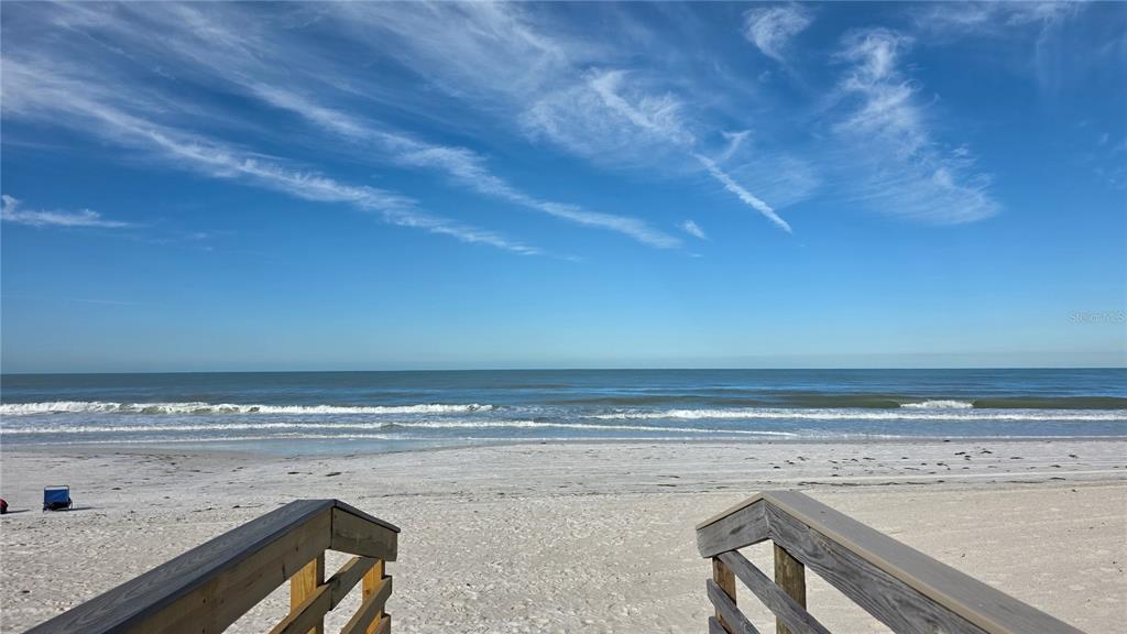 A wooden staircase leads down to a sandy beach overlooking the ocean under a blue sky — 531 BIRDIE LANE, LONGBOAT KEY, FL