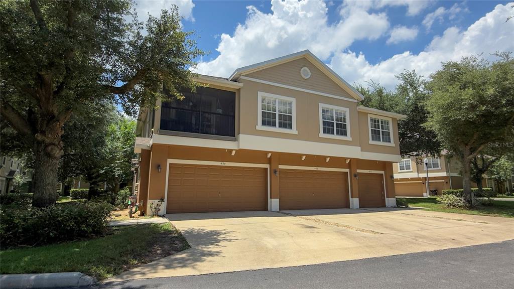 A two-story townhouse exterior features a tan facade, three garage doors, and a screened balcony — 494 ASHLEY BROOKE COURT UNIT A, APOPKA, FL