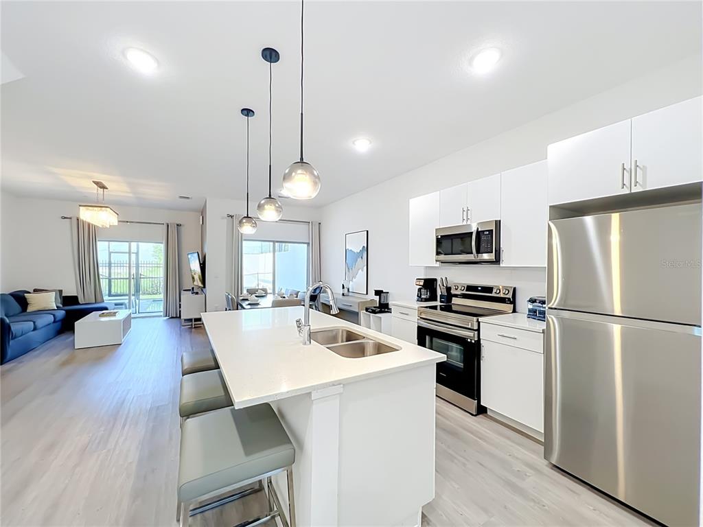 A modern kitchen with a white island and stainless steel appliances opens to a living area — 444 FAMAGUSTA DRIVE, DAVENPORT, FL