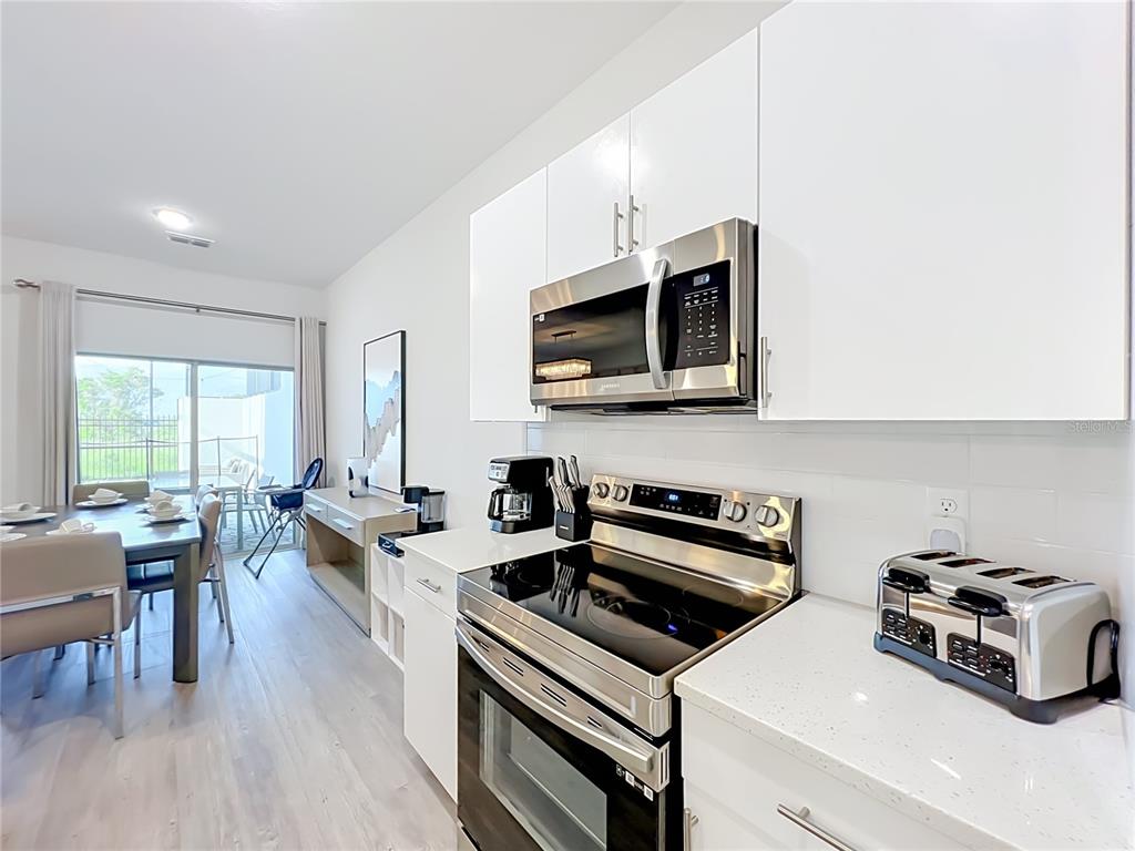 A modern kitchen features white cabinets, stainless steel appliances, and an adjacent dining area — 444 FAMAGUSTA DRIVE, DAVENPORT, FL