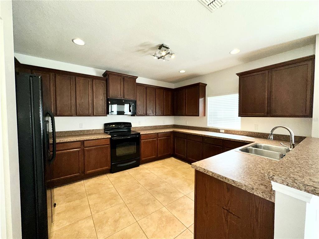 A kitchen with dark wood cabinets, laminate countertops, black appliances, and light tile flooring — 4612 CABALERRO TRAIL, KISSIMMEE, FL