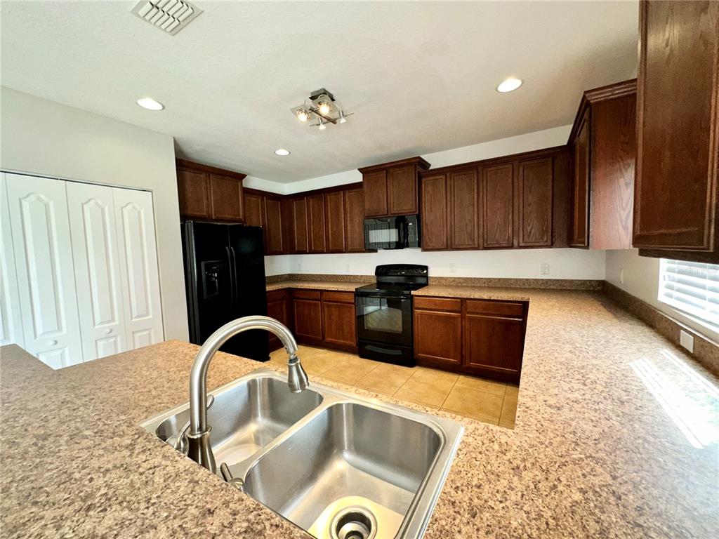 A kitchen features dark wood cabinets, speckled laminate countertops, and black appliances — 4612 CABALERRO TRAIL, KISSIMMEE, FL