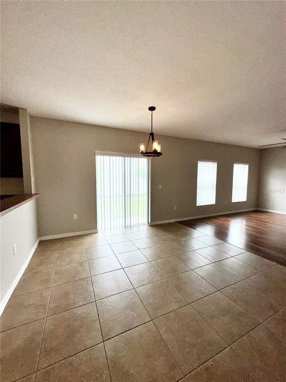 A room with light-colored tile flooring, a hanging light fixture, and sliding glass doors — 4612 CABALERRO TRAIL, KISSIMMEE, FL