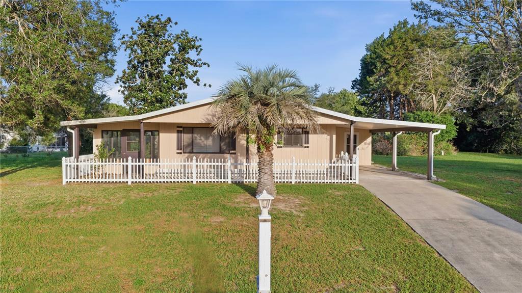 A single-story house with beige siding, a white picket fence, and a carport — 10040 SW 98TH AVENUE, OCALA, FL