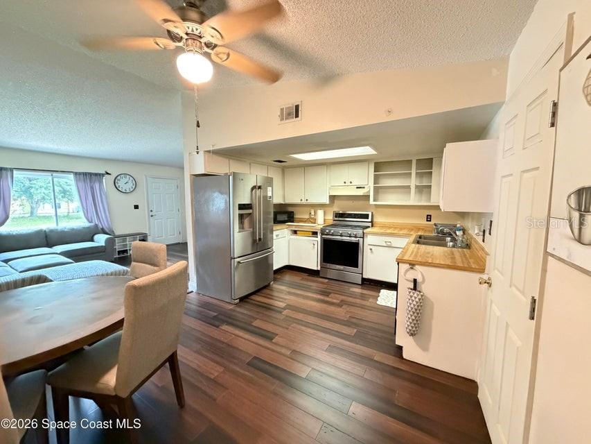 An open-concept kitchen features white cabinets, stainless steel appliances, and wood-look flooring — 1578 W POWDER HORN ROAD, TITUSVILLE, FL