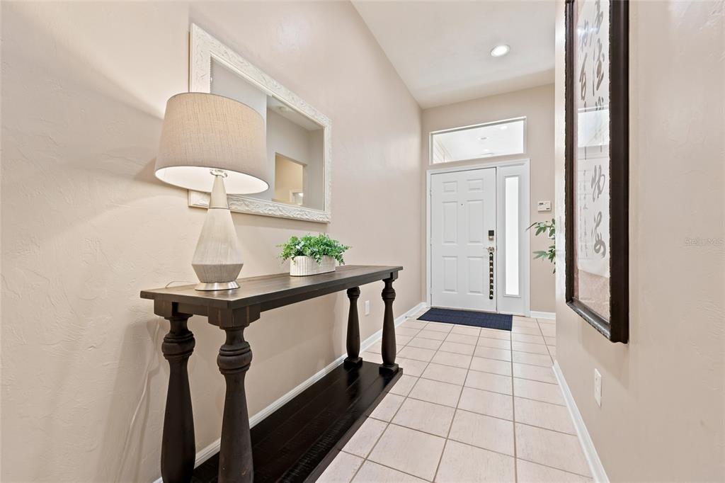 An entryway features a dark wood console table, a lamp, a mirror, and tiled flooring — 9408 SW 39TH AVENUE, GAINESVILLE, FL