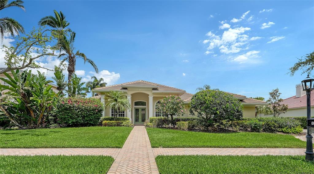 A single-story house with a paved walkway, green lawn, and palm trees under a blue sky — 8923 BLOOMFIELD BOULEVARD, SARASOTA, FL