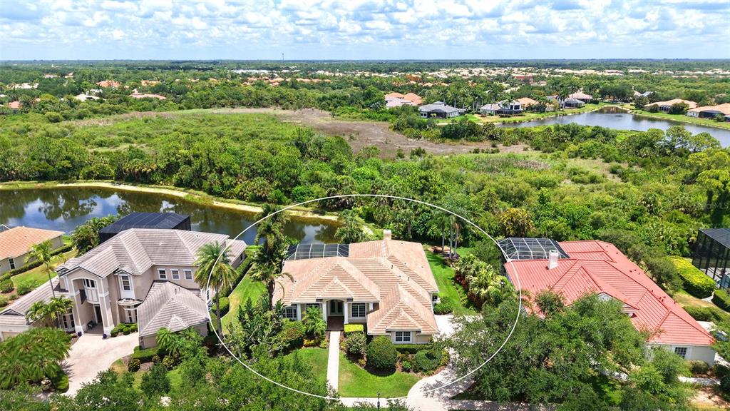 An aerial view shows a tan-roofed house surrounded by lush greenery and nearby ponds — 8923 BLOOMFIELD BOULEVARD, SARASOTA, FL