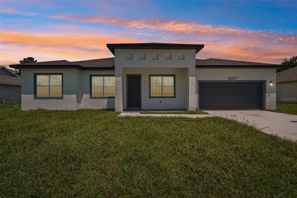 A single-story house with a gray garage, stucco exterior, and a front entrance at sunset — 6207 SW 128TH STREET ROAD, OCALA, FL