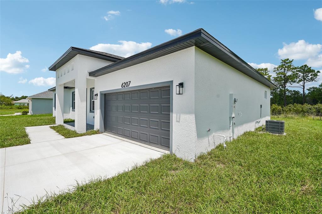 A modern, white stucco single-story house features a gray garage door and a concrete driveway — 6207 SW 128TH STREET ROAD, OCALA, FL