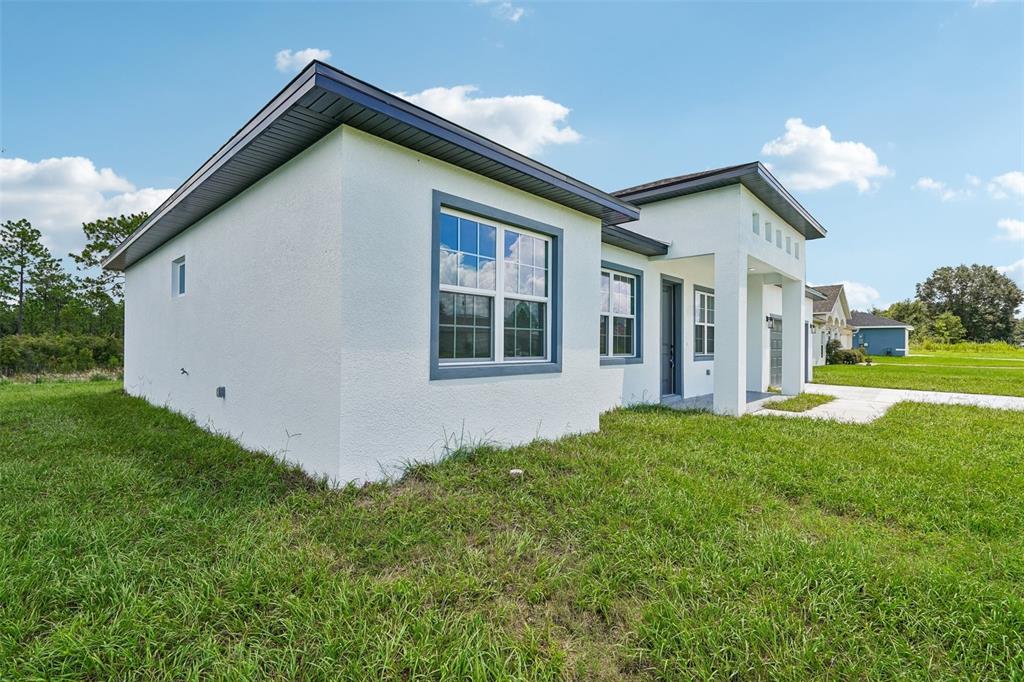 A side view of a white stucco house with a dark roof and gray trim — 6207 SW 128TH STREET ROAD, OCALA, FL